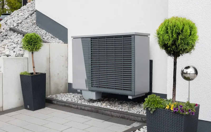 Unité extérieure de pompe à chaleur installée sur une terrasse gravillonnée entre deux plantes en pot