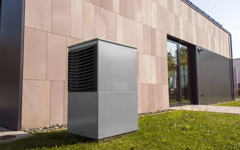 Pompe à chaleur air-eau posée sur la pelouse devant la façade d'une maison moderne