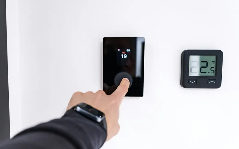 Main réglant la température sur un thermostat d'ambiance mural